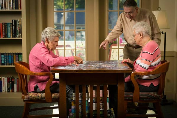 Three residents engaging in a puzzle activity at a table in a common area.