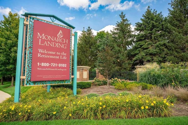 Welcome sign for Monarch Landing retirement community with flowers and greenery