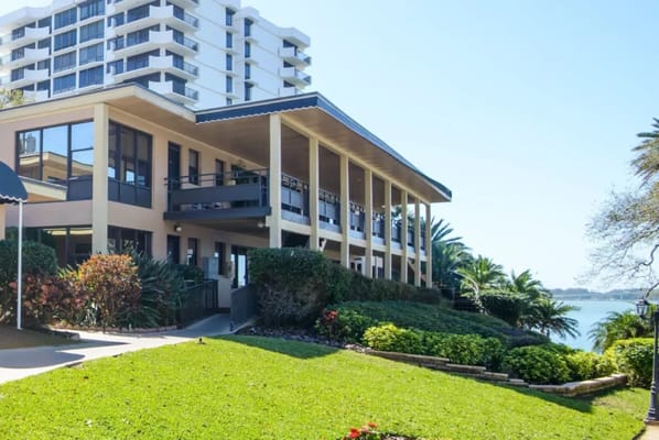 The Oaks of Clearwater senior living facility exterior with palm trees and waterfront view.