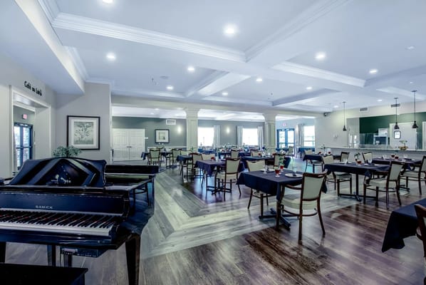 A spacious dining room with tables and a grand piano.