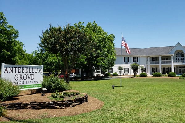 Front view of Antebellum Grove Senior Living facility with sign and flag