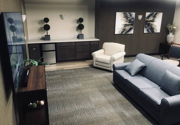 A cozy living room featuring a blue couch, white armchair, and decorative plants.