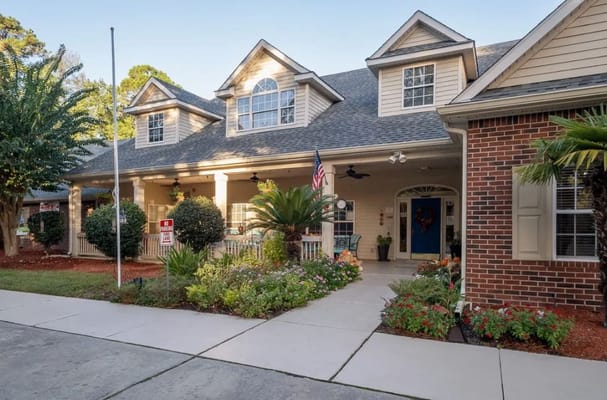 Front entrance of Village Cove Assisted Living with gardens and American flag.