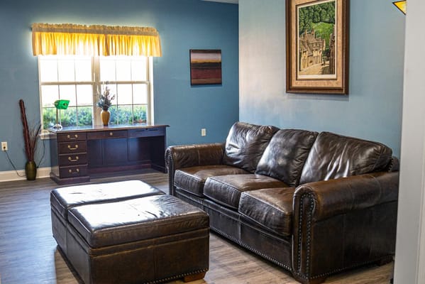 A cozy living room with a leather couch, coffee table, and sunny windows.