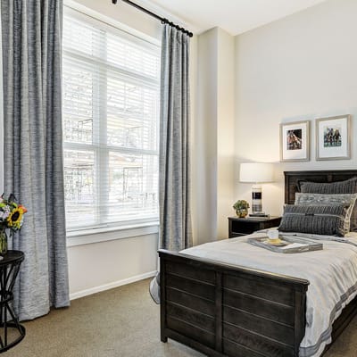 Neatly arranged bed with decorative pillows and a side table in a senior living bedroom.