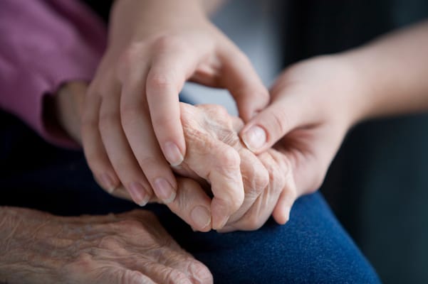 A caregiver holding the hand of an elderly person
