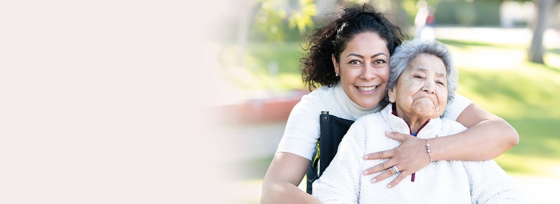 A caregiver hugging an elderly resident in a garden setting