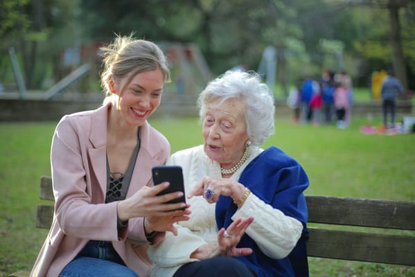 A staff member showing a resident something on a phone in a park