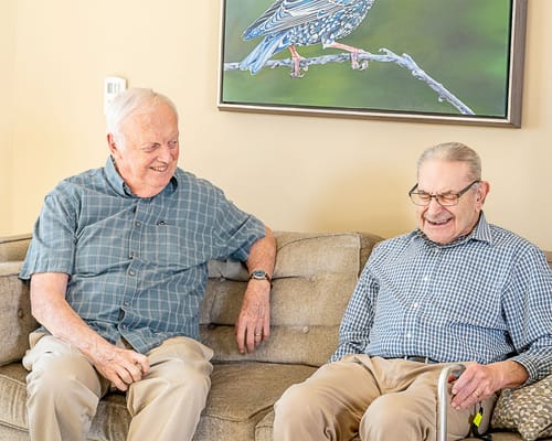 Two elderly men smiling and chatting in a common area