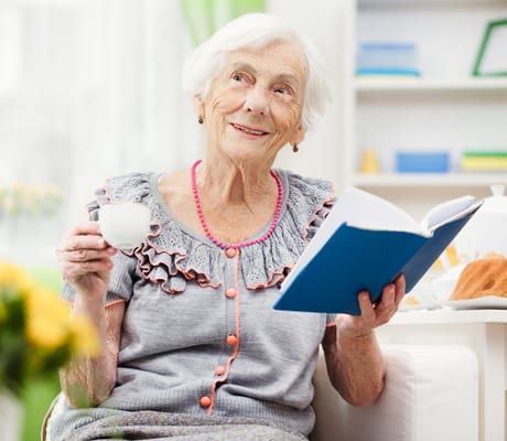 Elderly resident enjoying a book and tea in a cozy setting