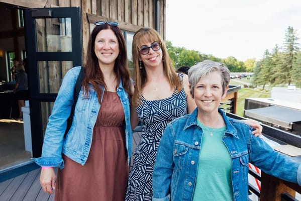 Three women smiling outdoors at an event