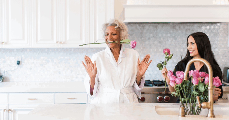 Two women in a cheery kitchen holding flowers