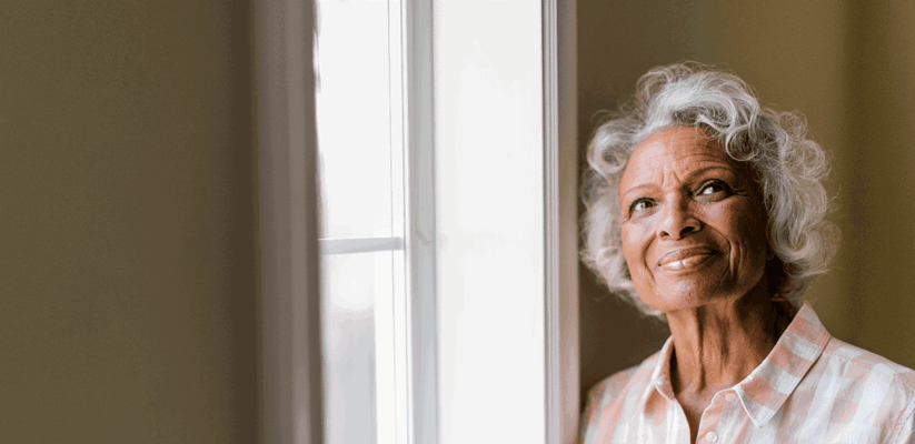 A smiling elderly woman gazing out a window