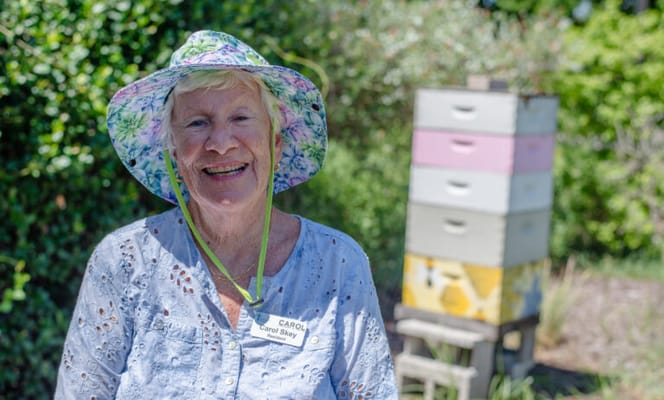 Resident smiling in the garden with bee boxes in background
