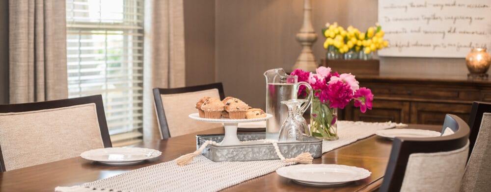 A dining room table set with muffins and flowers