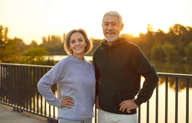 Two smiling seniors by a lake during sunset