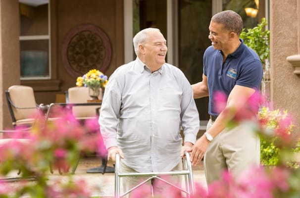 A caregiver assists a resident outside in a garden area