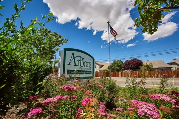 Sign of Arbors Memory Care surrounded by flowers and greenery.