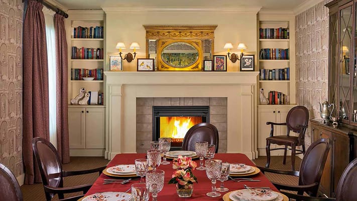 Dining room with a red tablecloth, elegant table setting, and a fireplace.