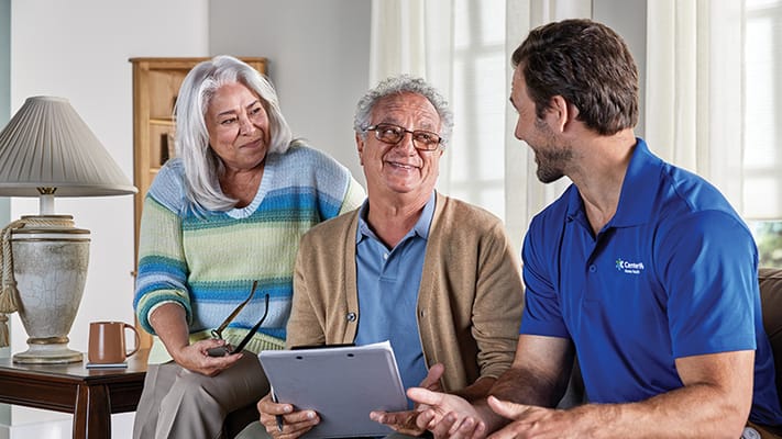 Two seniors interacting with a caregiver in a living room.