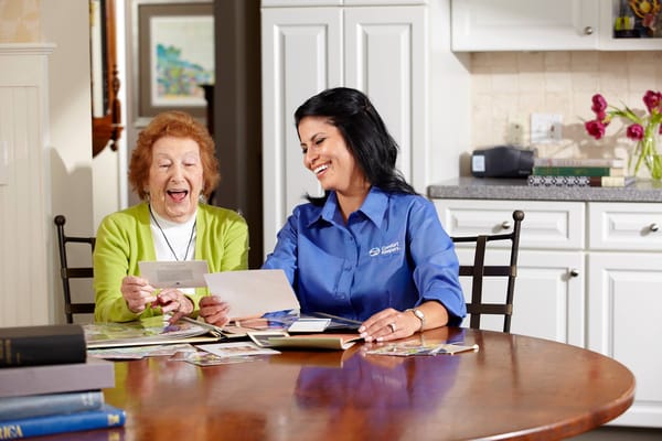 A caregiver and a senior woman joyfully looking at photographs together.