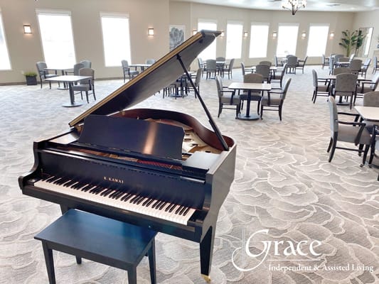 A Kawai grand piano in a spacious common area with tables and chairs.