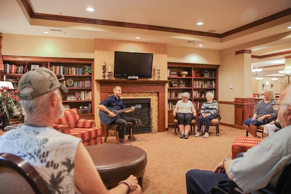A musician performing with a guitar for residents in a cozy lounge area