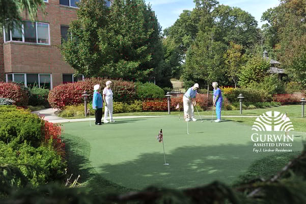 Seniors playing on the putting green surrounded by colorful landscaping.