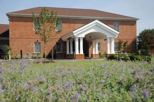 The front entrance of Harrison House of Georgetown, featuring a brick building and landscaped surroundings.
