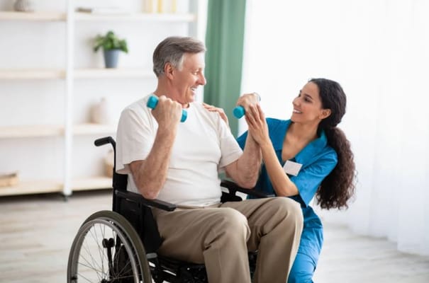 Senior man in a wheelchair smiling while exercising with a caregiver.