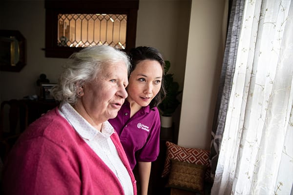 A caregiver and a senior looking out of a window together