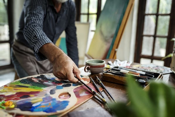 A close-up of a person holding a paintbrush over a colorful palette.