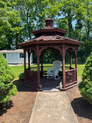 Wooden gazebo with a rocking chair surrounded by greenery