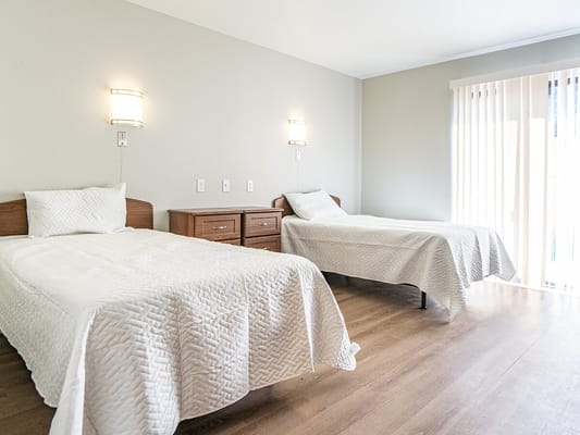 A spacious bedroom with two beds and natural light from a window.