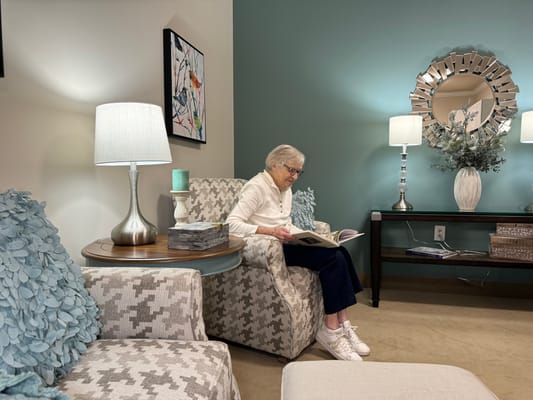Senior woman reading a book in a comfortable sitting area with lamps and decor.