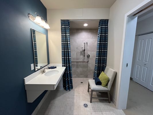A modern bathroom with a shower, sink, and a chair.