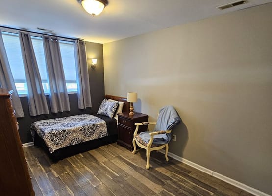 A neatly arranged bedroom featuring a bed, nightstand, and chair.