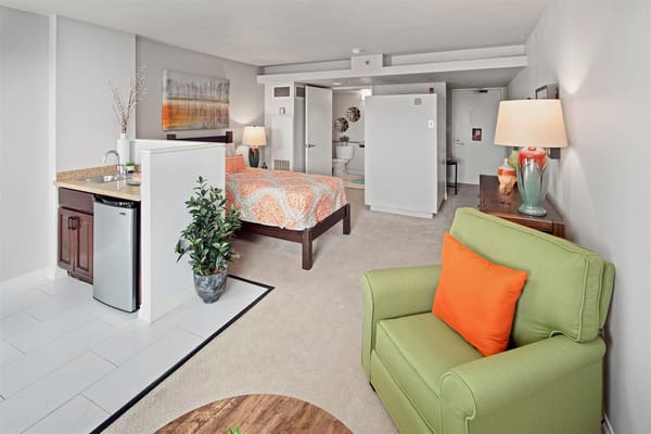 Interior view of a comfortable senior living room with a bed, kitchenette, and seating area.