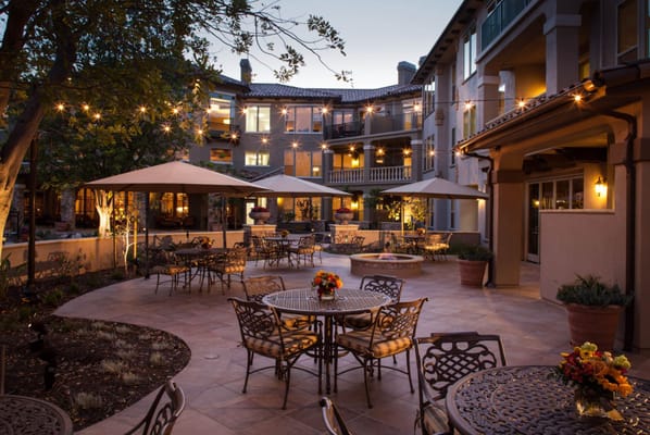 An outdoor patio with tables and umbrellas illuminated by string lights.