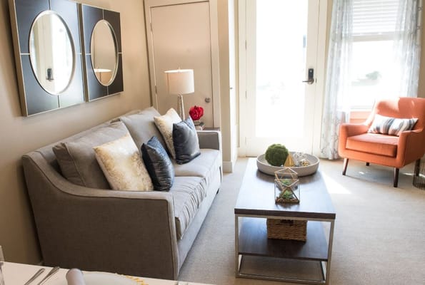 Modern living room with grey sofa, orange chair, and decorative table.