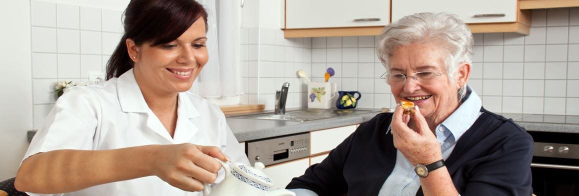 Caregiver serving tea to a senior resident in the kitchen