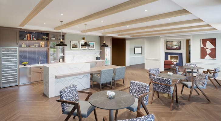 A modern common area with tables, chairs, and a kitchenette in Sunrise of Killarney.