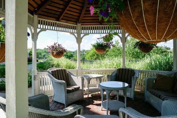 Seating area under gazebo with hanging flower pots.