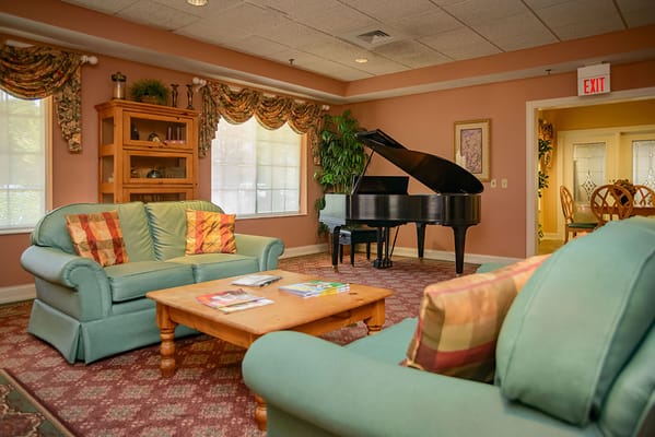 Lounge area features green sofas, a grand piano, and a coffee table with magazines.