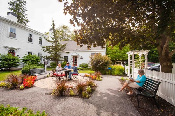 Three residents gathered around a table in a garden, with one person sitting on a bench reading.