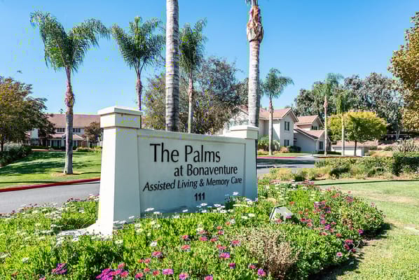 Sign for The Palms at Bonaventure Senior Living surrounded by flowers and palm trees