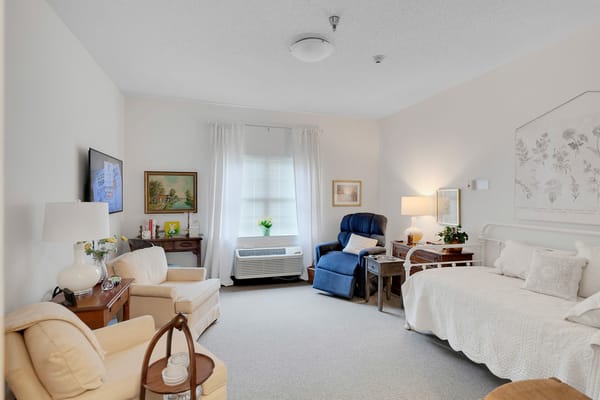 Private bedroom featuring a bed, seating area, and window with curtains.