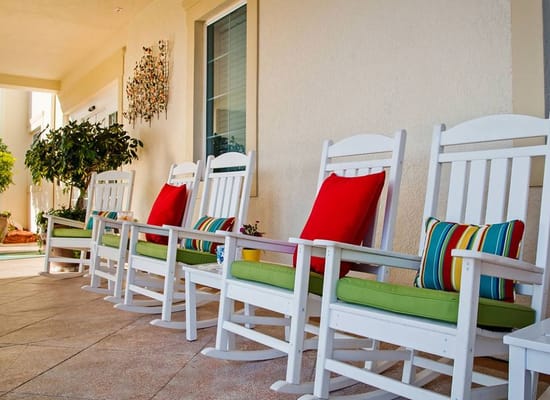 Row of white rocking chairs with colorful cushions on a porch