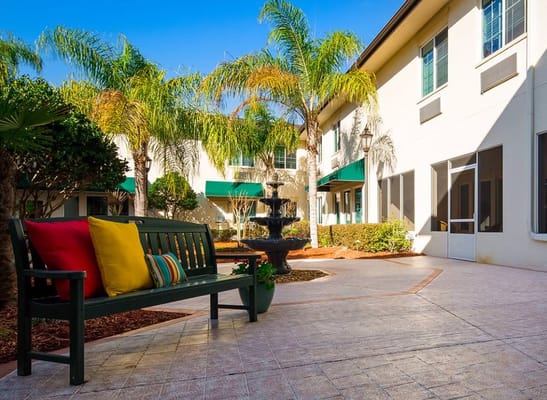 A peaceful courtyard with a bench and fountain surrounded by palm trees.