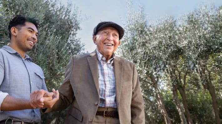 A senior man walking outside with a caregiver